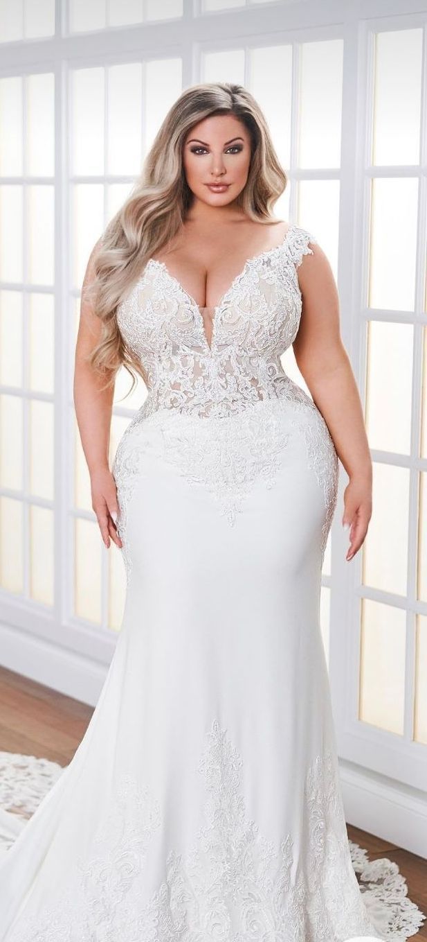 Woman in a white bridal gown with lace bodice and flowing skirt, standing in front of a window.