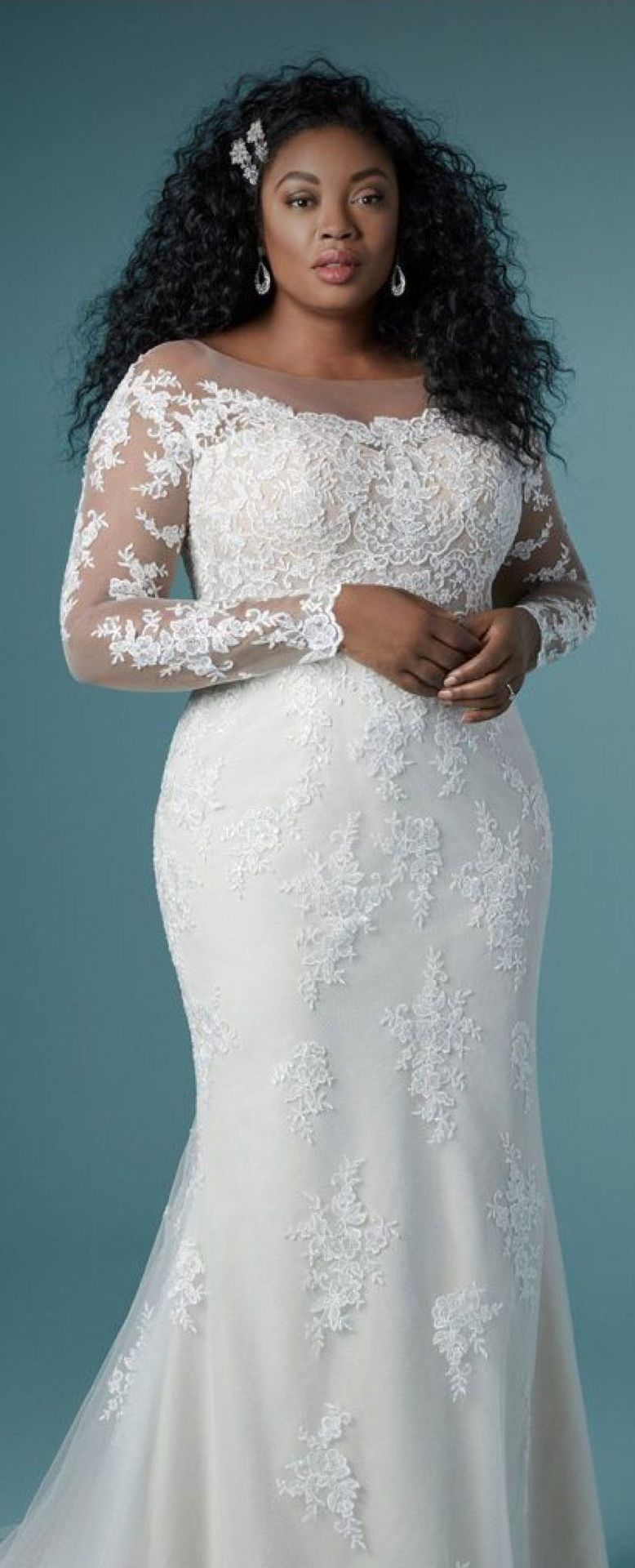 Woman in a white lace wedding dress with long sleeves and a mermaid skirt, smiling.