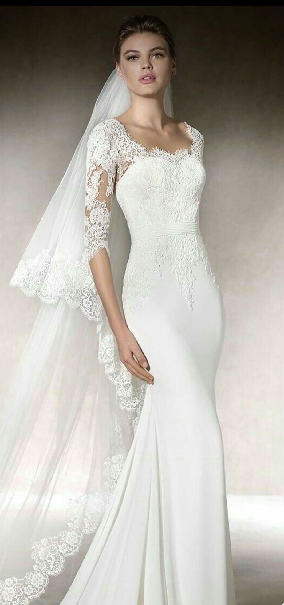 Woman wearing a white wedding dress with lace sleeves and a long veil.