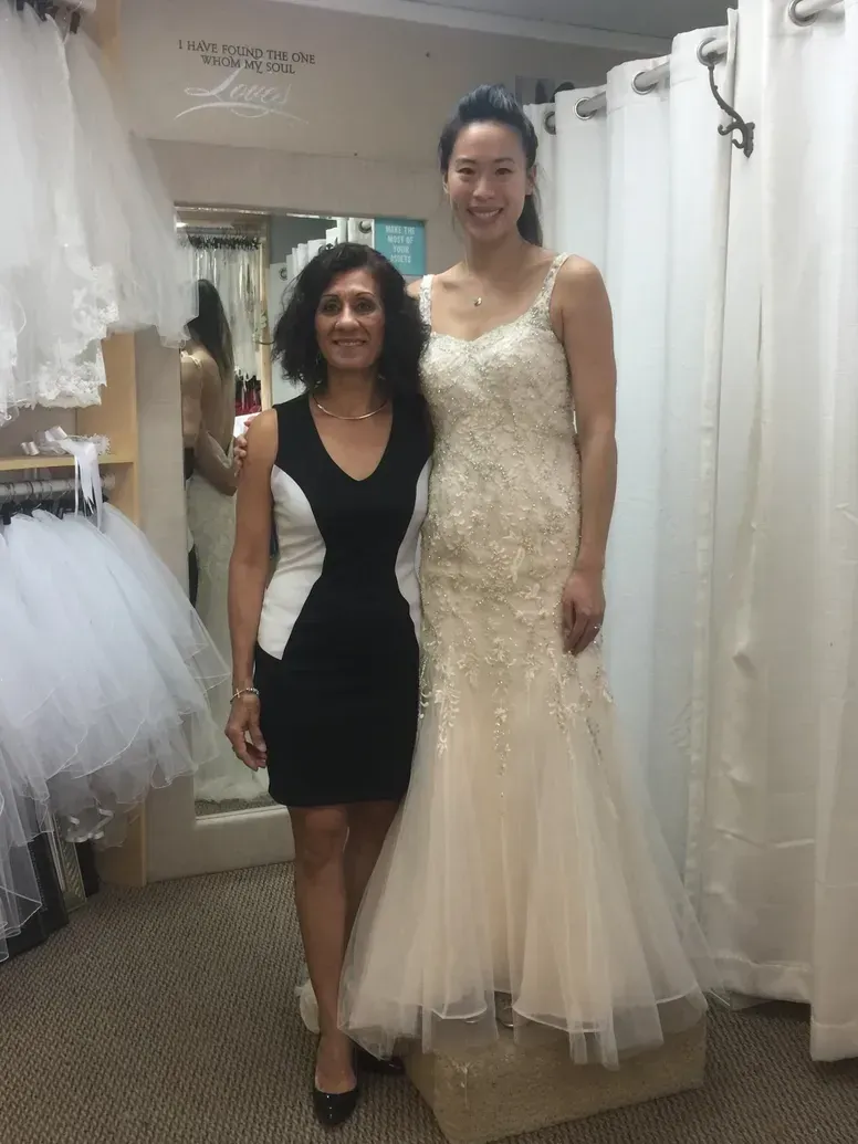 Woman in wedding dress stands with woman in black and white dress in bridal shop.