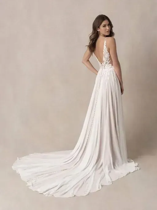 Woman in a white wedding dress with a long train, turned towards the viewer, smiling.