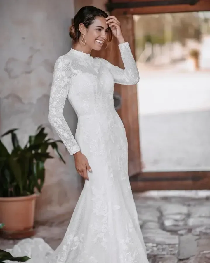 Woman in white lace wedding dress, smiling, indoors.