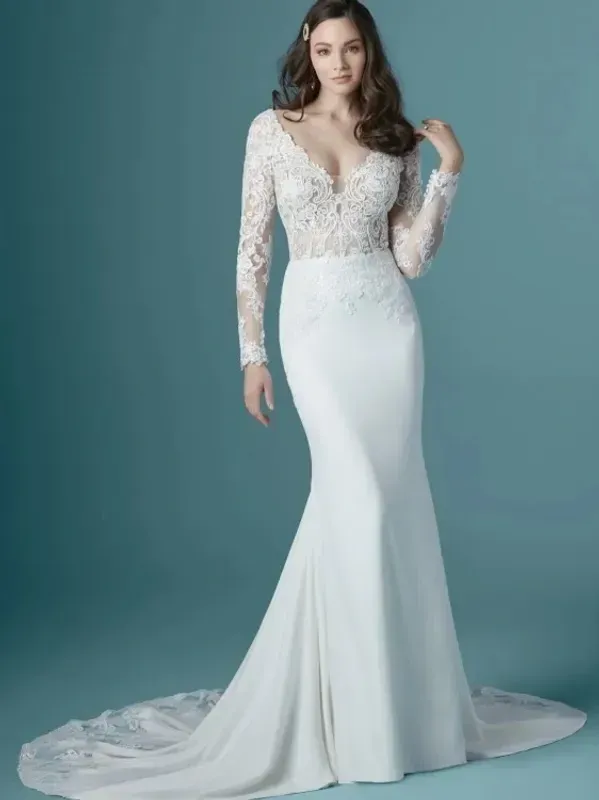 Woman in a white lace and crepe wedding dress with a long train, posed against a teal background.