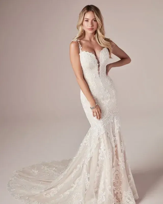 Woman in a white lace mermaid wedding dress, posing in a studio with a train.