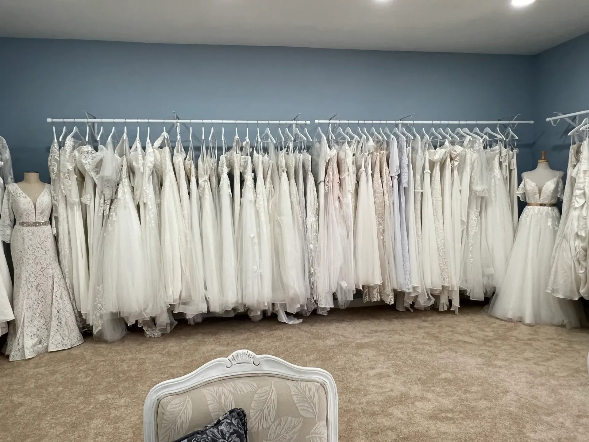 Wedding dresses hanging in a bridal boutique with neutral-colored carpet and blue walls.