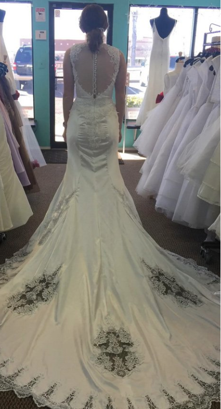 Woman in white wedding dress with lace detail and long train in a bridal shop.