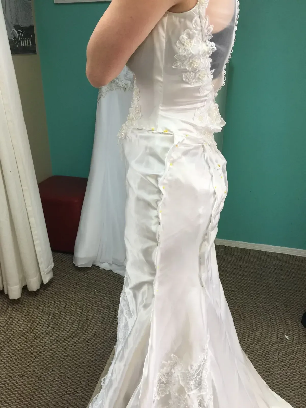 Woman in a white wedding dress trying it on in a bridal shop. Teal wall in the background.