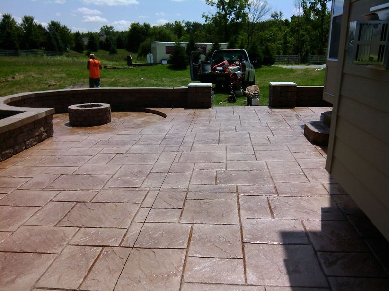Stamped concrete patio with a fire pit, next to a building and a field with a truck.