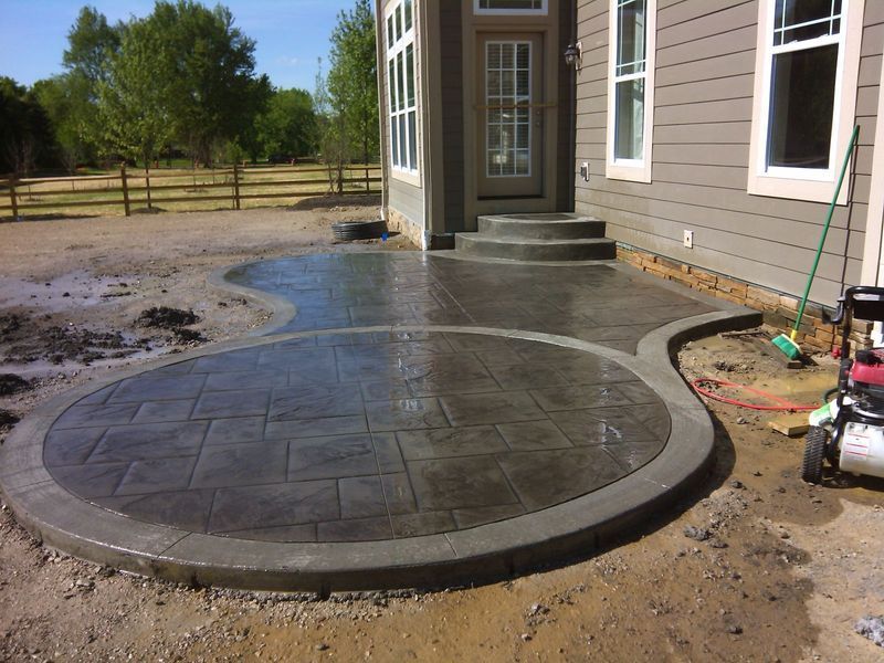 Newly poured gray concrete patio with textured surface next to a house with steps.