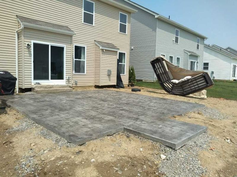 Backyard patio under construction with sliding door, grey concrete, and outdoor chair.