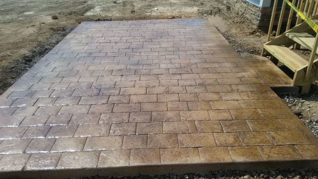 Concrete patio with stamped brick pattern in shades of brown. Small wooden stairs to the right.