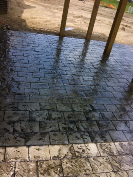 Stamped concrete patio with a brick pattern, gray tones, and wooden support beams.