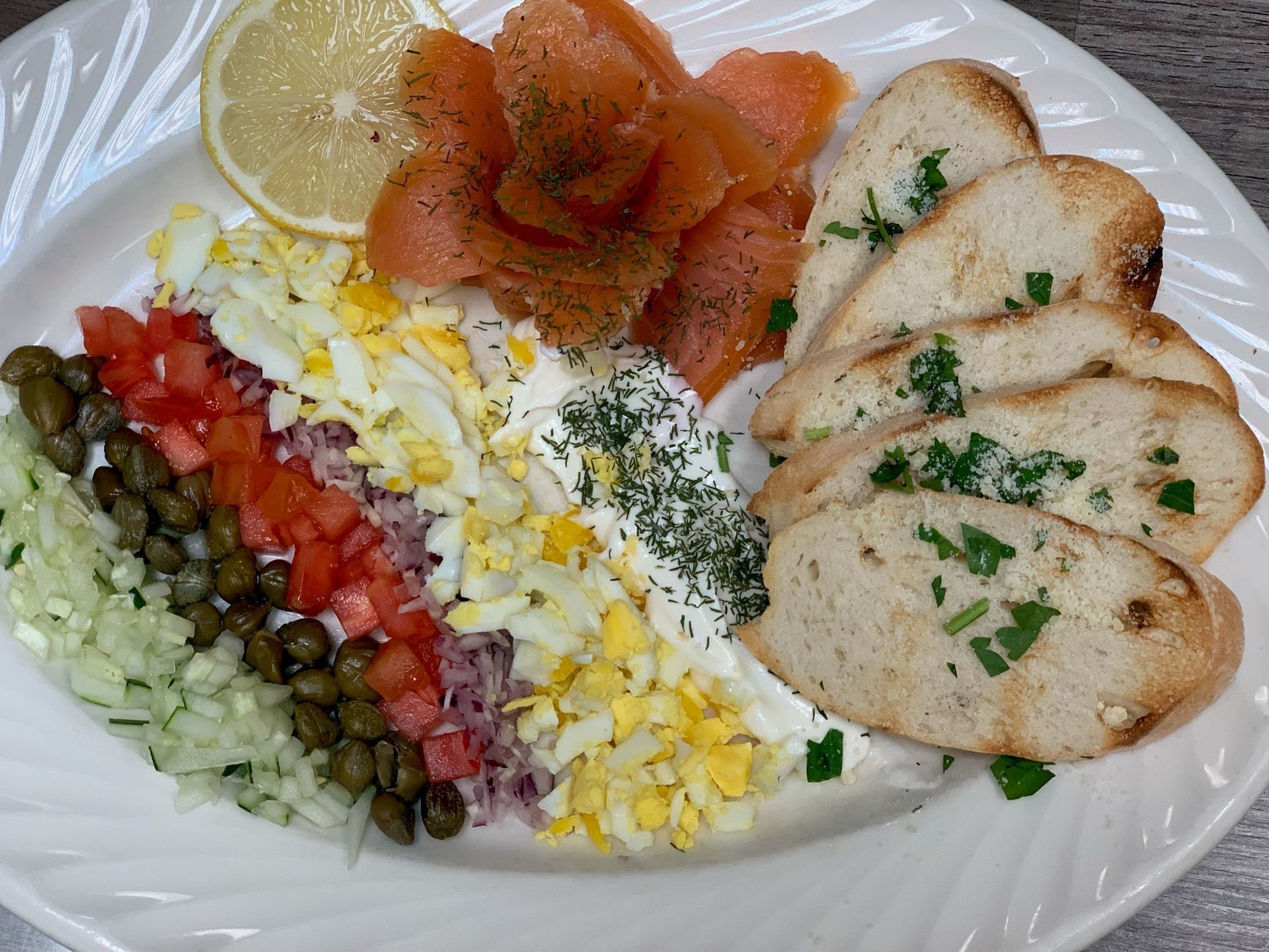 Assorted salad with sliced chicken, smoked salmon, capers, lemon, diced vegetables, and herbed garnish on a plate