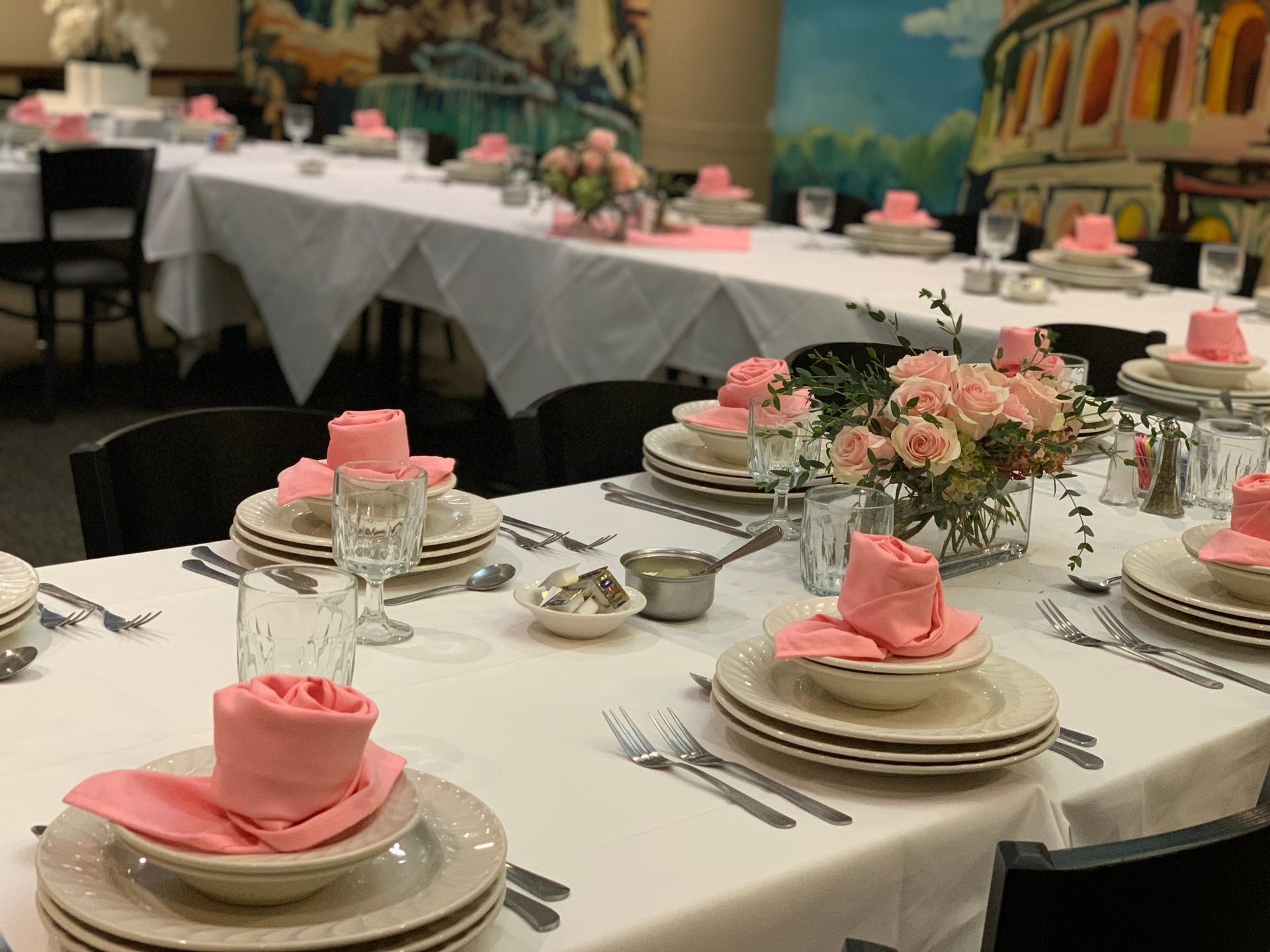 Elegant banquet tables with pink napkins, plates, glassware, and floral centerpieces in a formal dining room