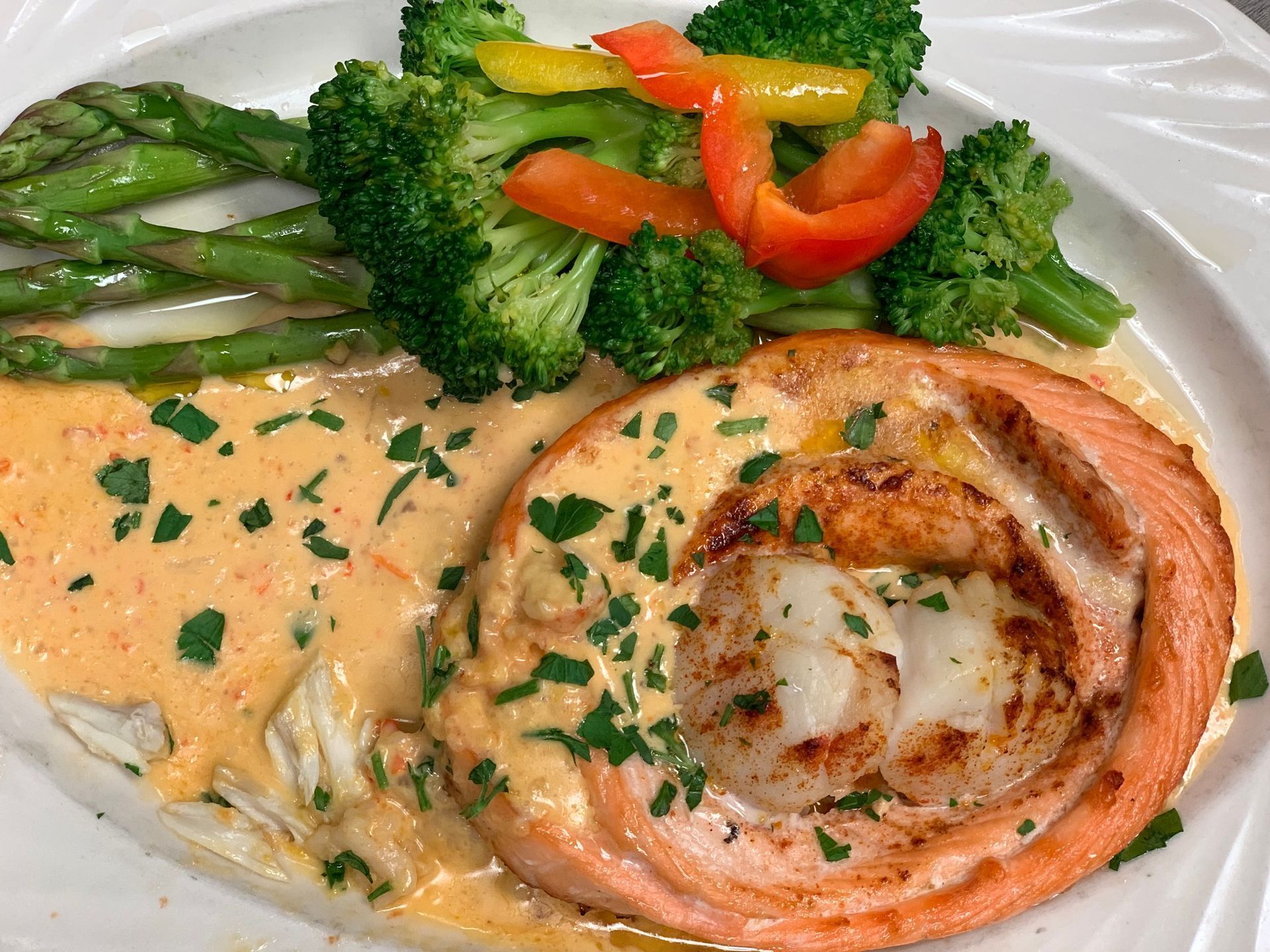 Plated salmon with creamy sauce, broccoli, asparagus, and red bell pepper garnish