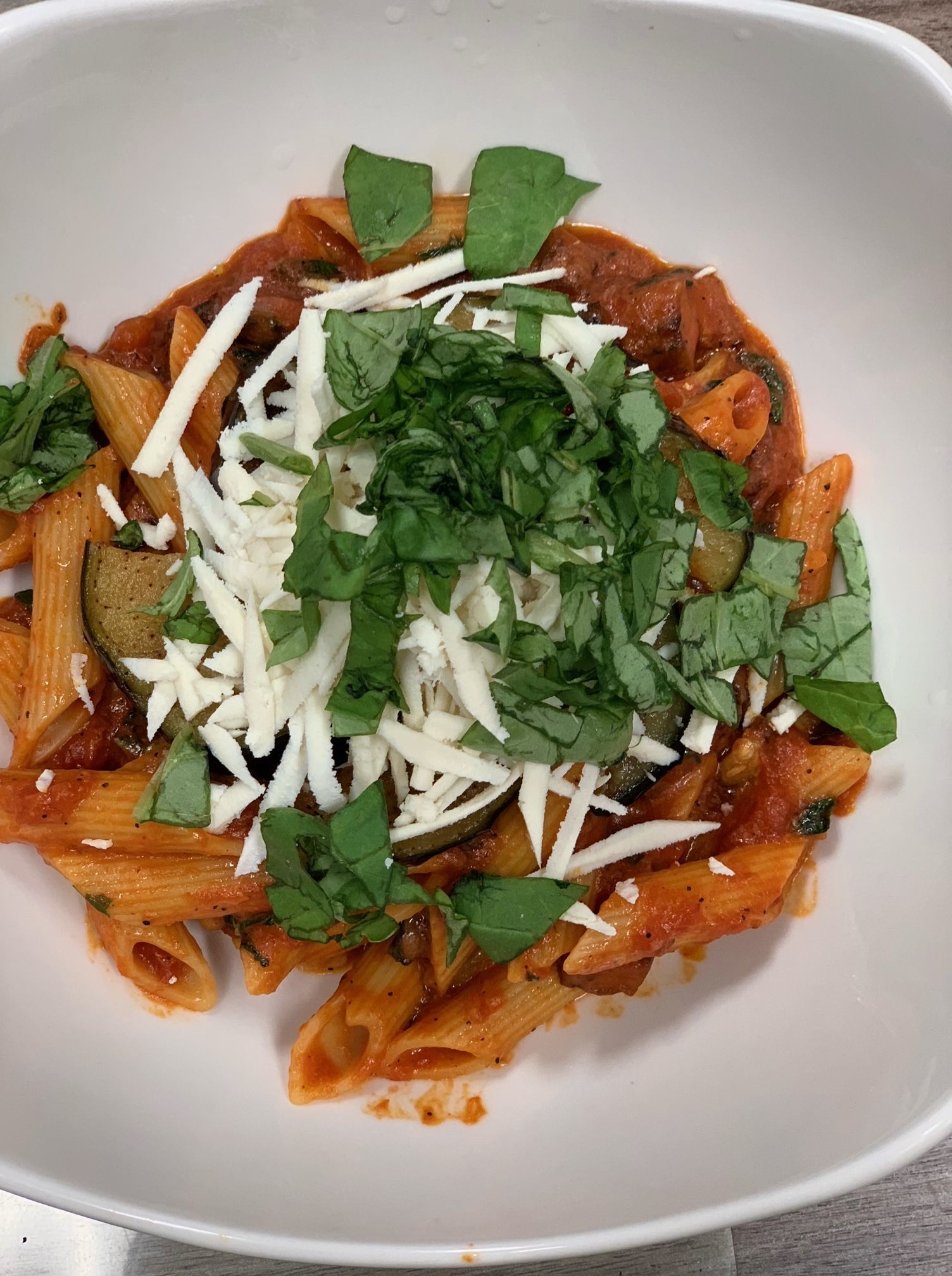 Penne pasta in red sauce topped with shaved cheese and basil in a white bowl