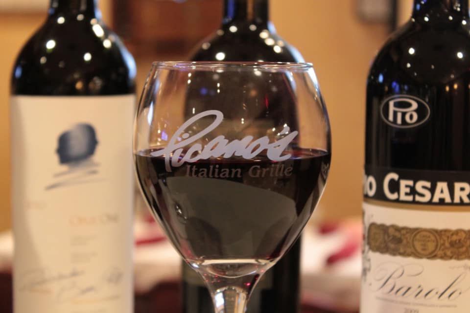 Wine glass on a table between two wine bottles in a softly lit restaurant setting