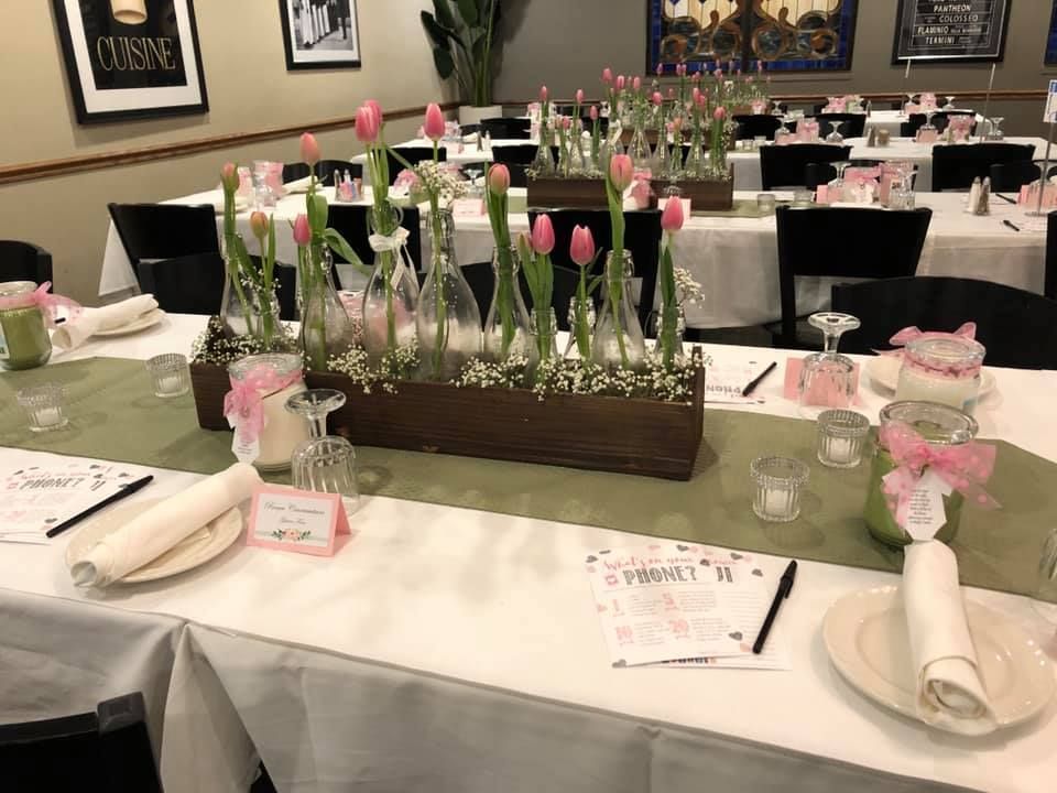 Banquet table centerpiece with pink flowers, candles, and place settings in a decorated dining room