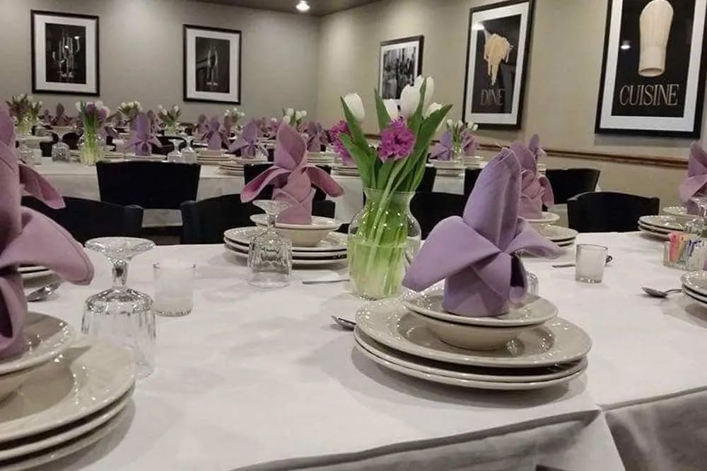 Elegantly set banquet table with white linens, purple napkins, glassware, and floral centerpieces in a dining hall