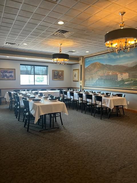 Empty banquet room with white tablecloths, black chairs, and large wall murals under warm chandeliers.