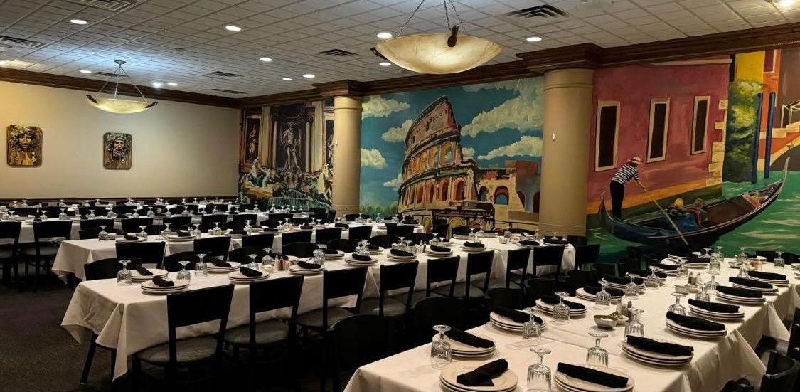 Elegant restaurant dining room with rows of white-clothed tables, chandeliers, and mural-covered walls