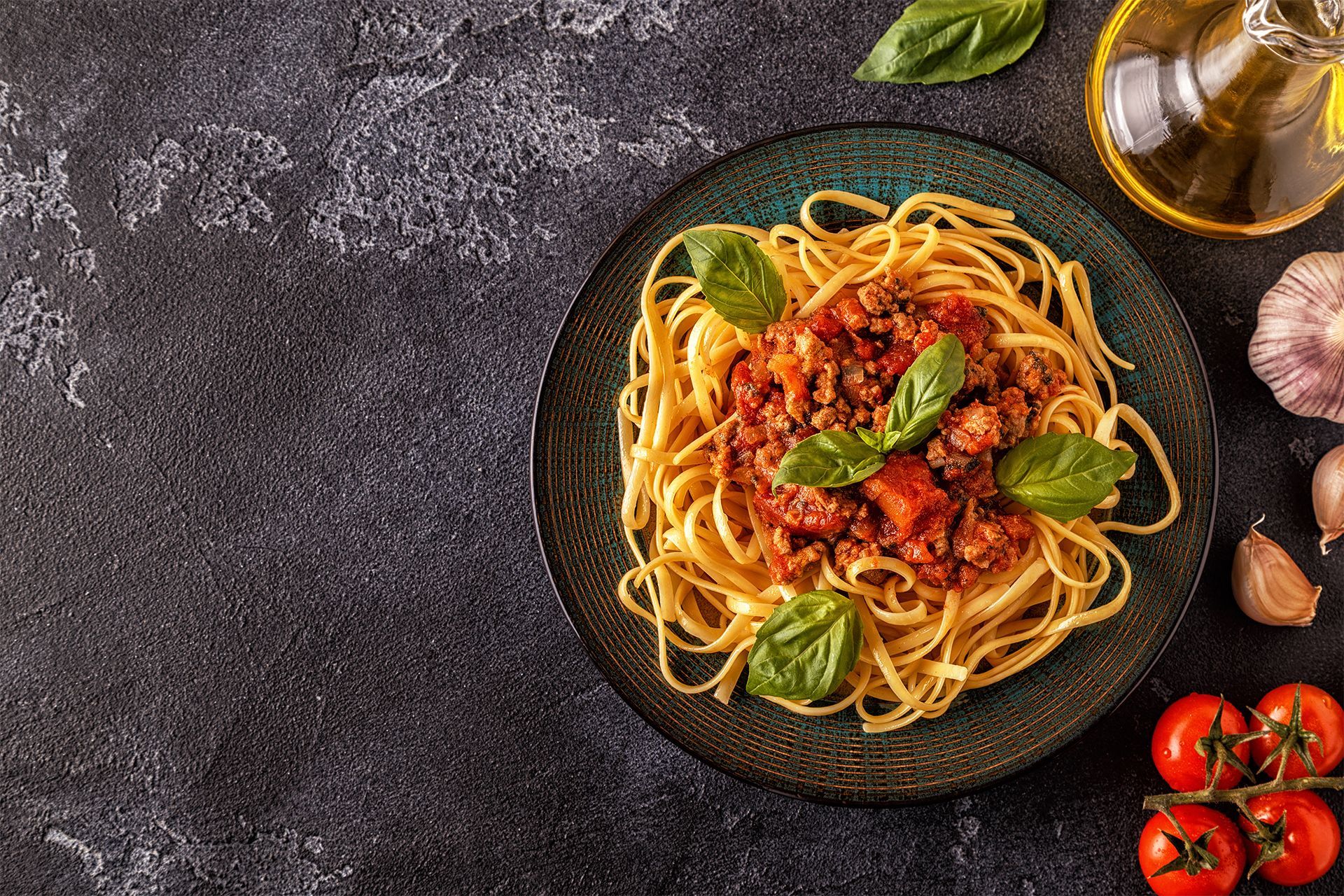 Pasta with tomato sauce and basil on a dark plate, with tomatoes, garlic, and olive oil nearby. Pasta with tomato sauce and basil on a dark plate, with tomatoes, garlic, and olive oil nearby.