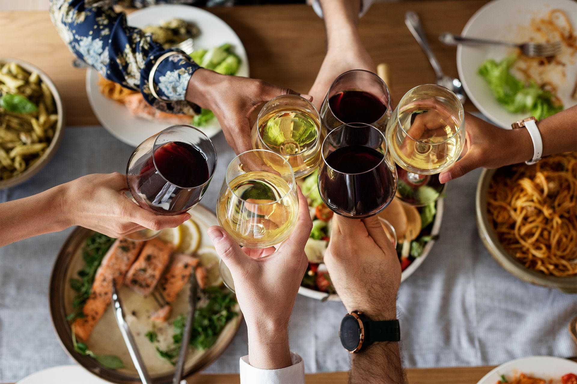 Hands raising glasses of red and white wine over a dinner table with pasta and seafood. Hands raising glasses of red and white wine over a dinner table with pasta and seafood.