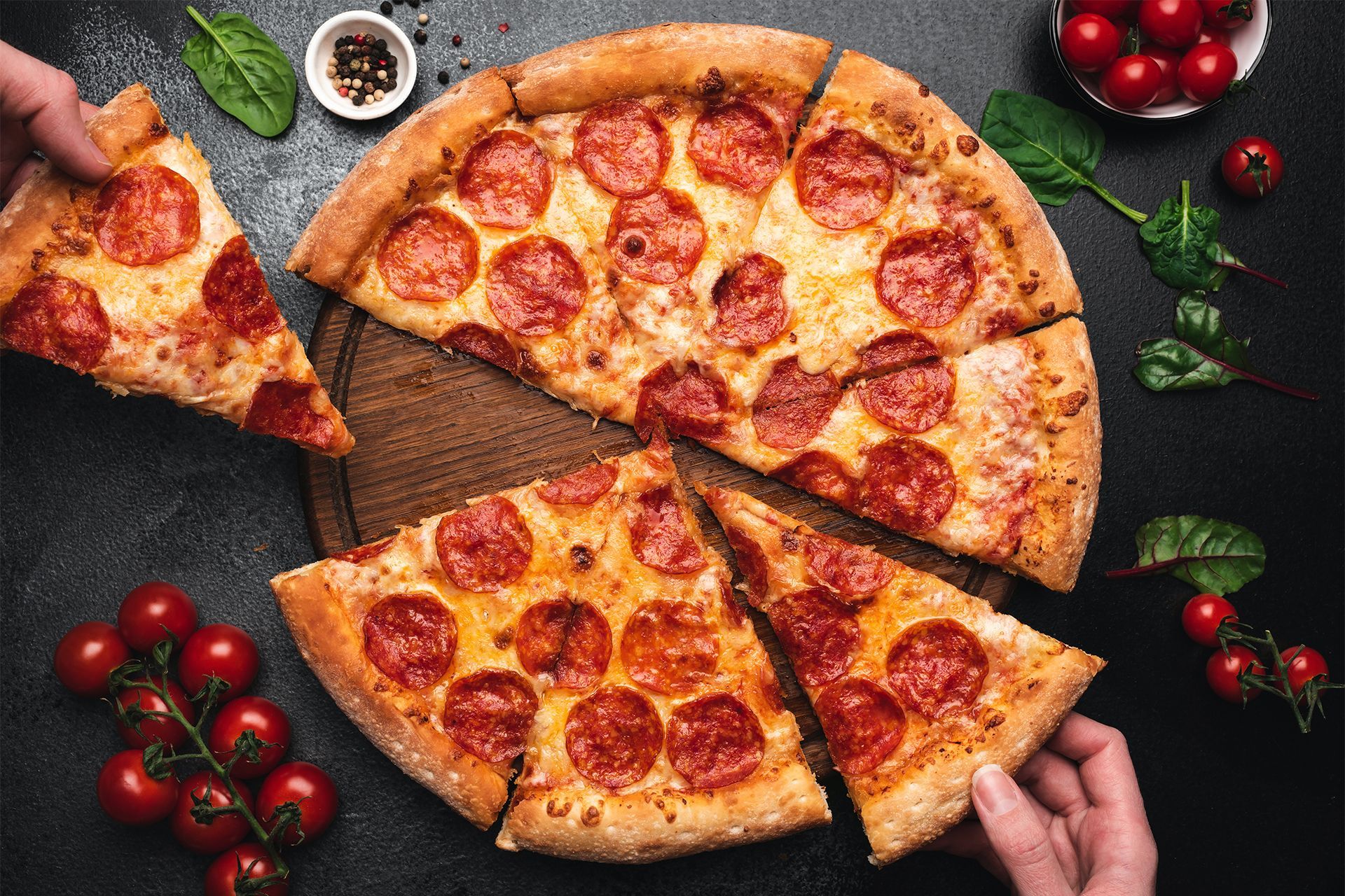 Top-down view of pepperoni pizza slices on a wooden board, with tomatoes, herbs, and dipping sauce around it. Top-down view of pepperoni pizza slices on a wooden board, with tomatoes, herbs, and dipping sauce around it.