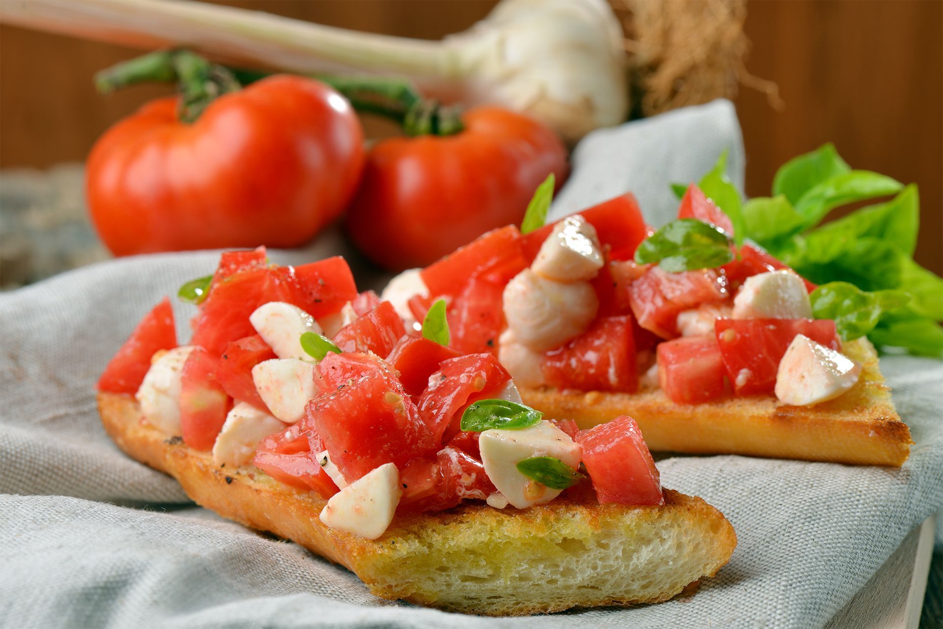 Tomato bruschetta on toasted bread with basil and mozzarella, with tomatoes in the background. Tomato bruschetta on toasted bread with basil and mozzarella, with tomatoes in the background.