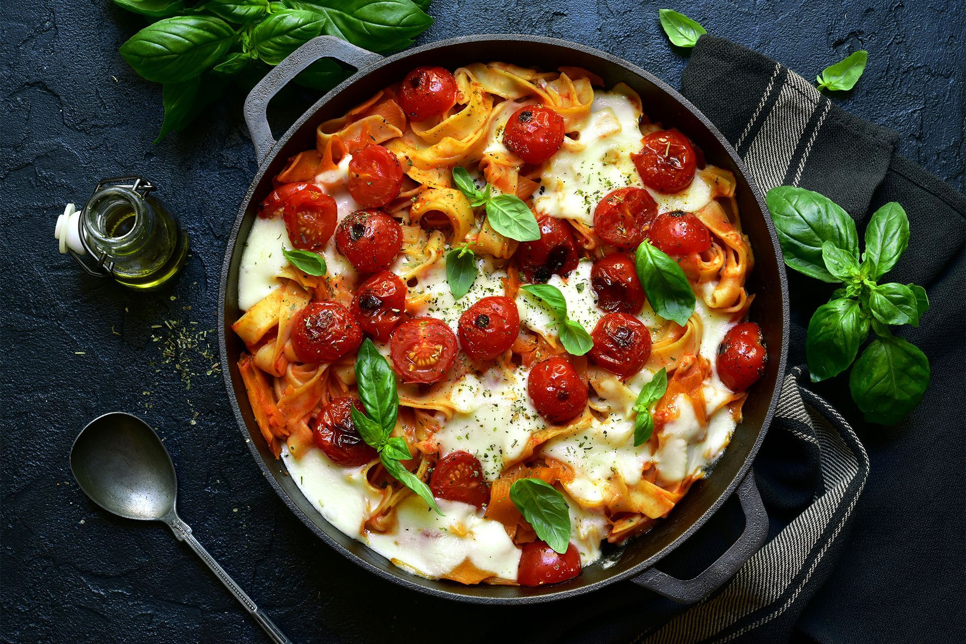 Skillet pizza topped with tomatoes, basil, and melted cheese on a dark table. Skillet pizza topped with tomatoes, basil, and melted cheese on a dark table.