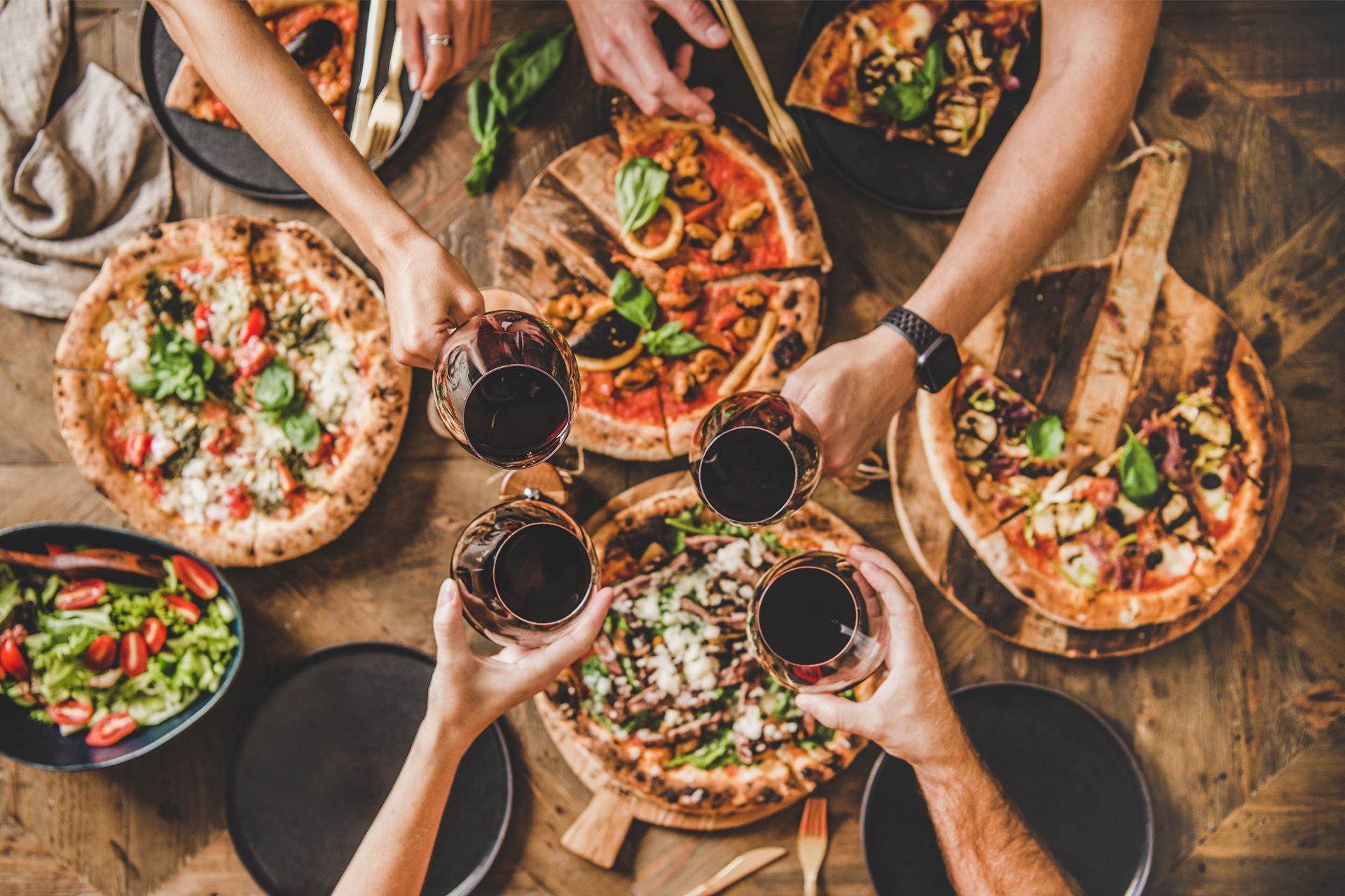 Friends sharing pizza and red wine around a rustic table overhead view.
