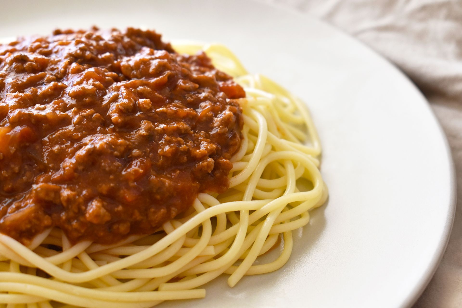 Plate of spaghetti topped with red meat sauce on a white plate. Plate of spaghetti topped with red meat sauce on a white plate.