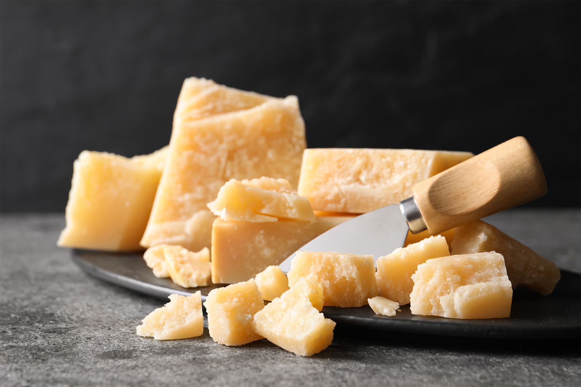 Cheese wedges and crumbles with a small knife on a dark surface.