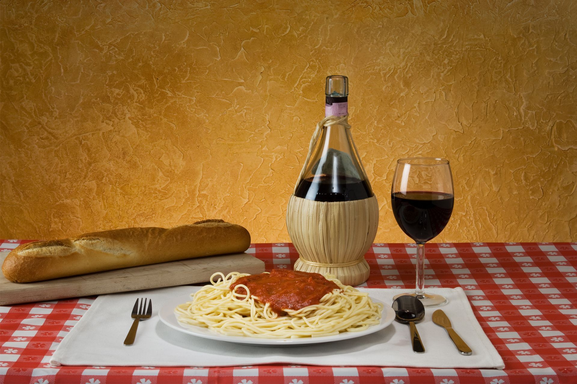 Pasta with tomato sauce, baguette, wine bottle and glass on a checkered tablecloth. Pasta with tomato sauce, baguette, wine bottle and glass on a checkered tablecloth.