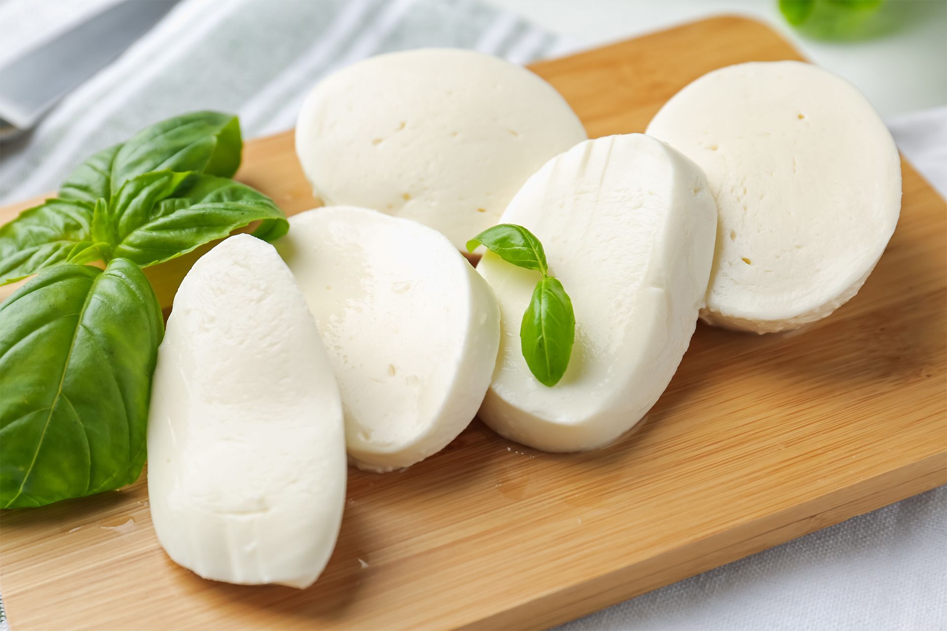 Sliced fresh mozzarella on a wooden board with basil leaves. Sliced fresh mozzarella on a wooden board with basil leaves.