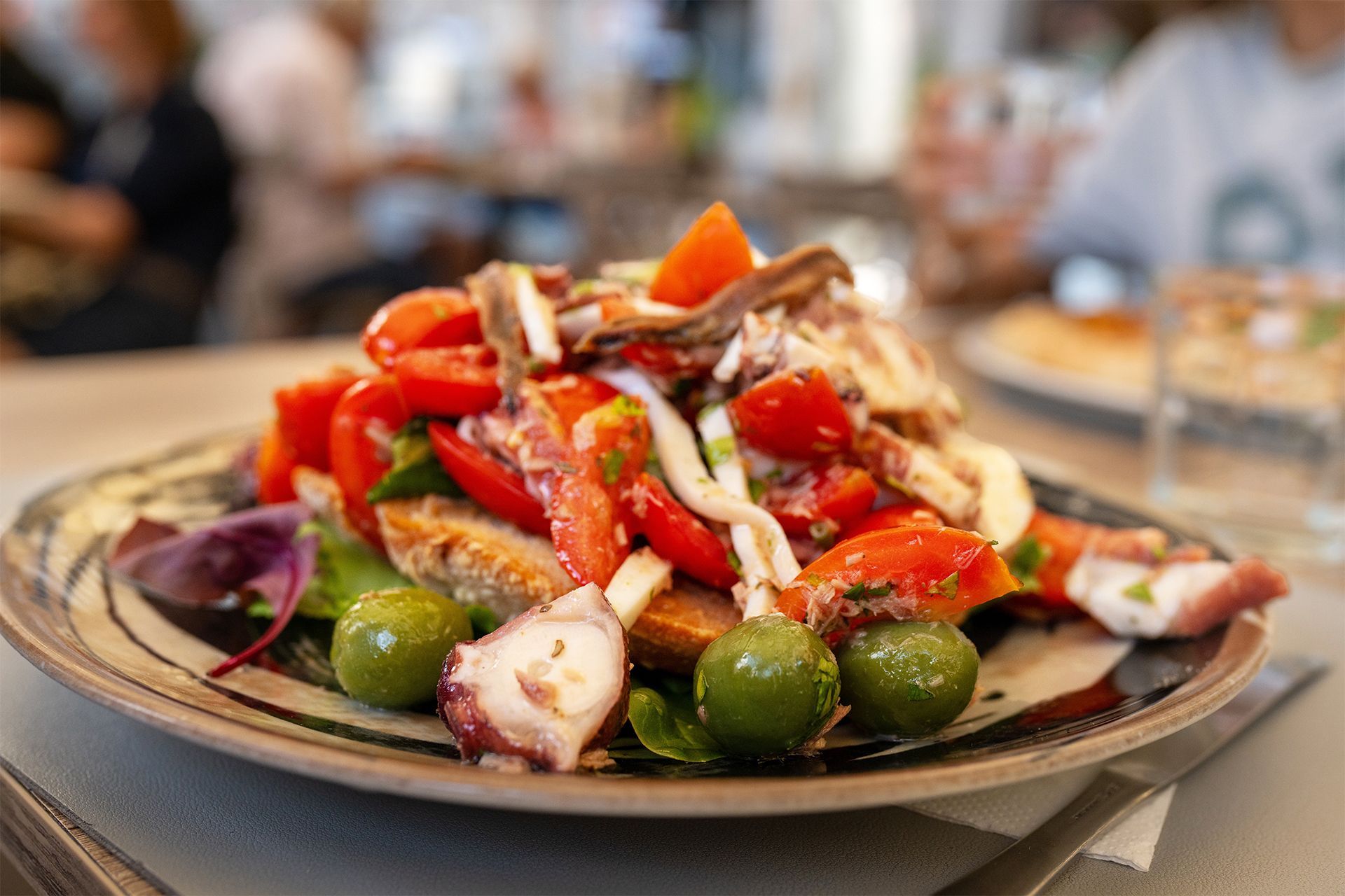 Plate of octopus salad with tomatoes, olives, and greens on a table. Plate of octopus salad with tomatoes, olives, and greens on a table.