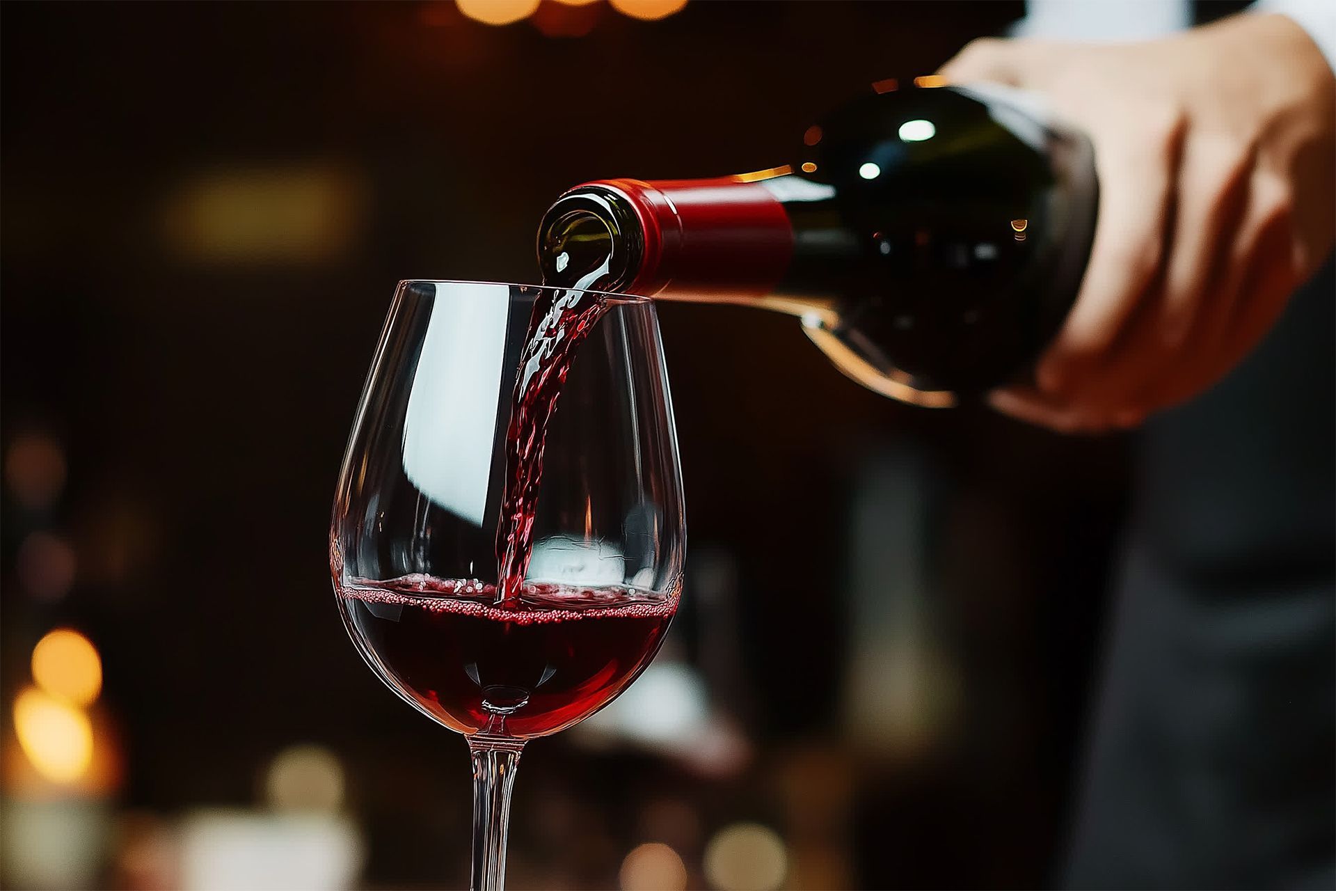 Red wine being poured into a wine glass in a dimly lit setting. Red wine being poured into a wine glass in a dimly lit setting.
