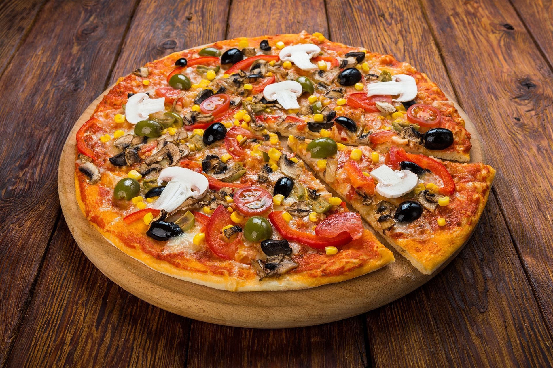 Pizza topped with olives, peppers, mushrooms, and cheese on a wooden board against a rustic table. Pizza topped with olives, peppers, mushrooms, and cheese on a wooden board against a rustic table.