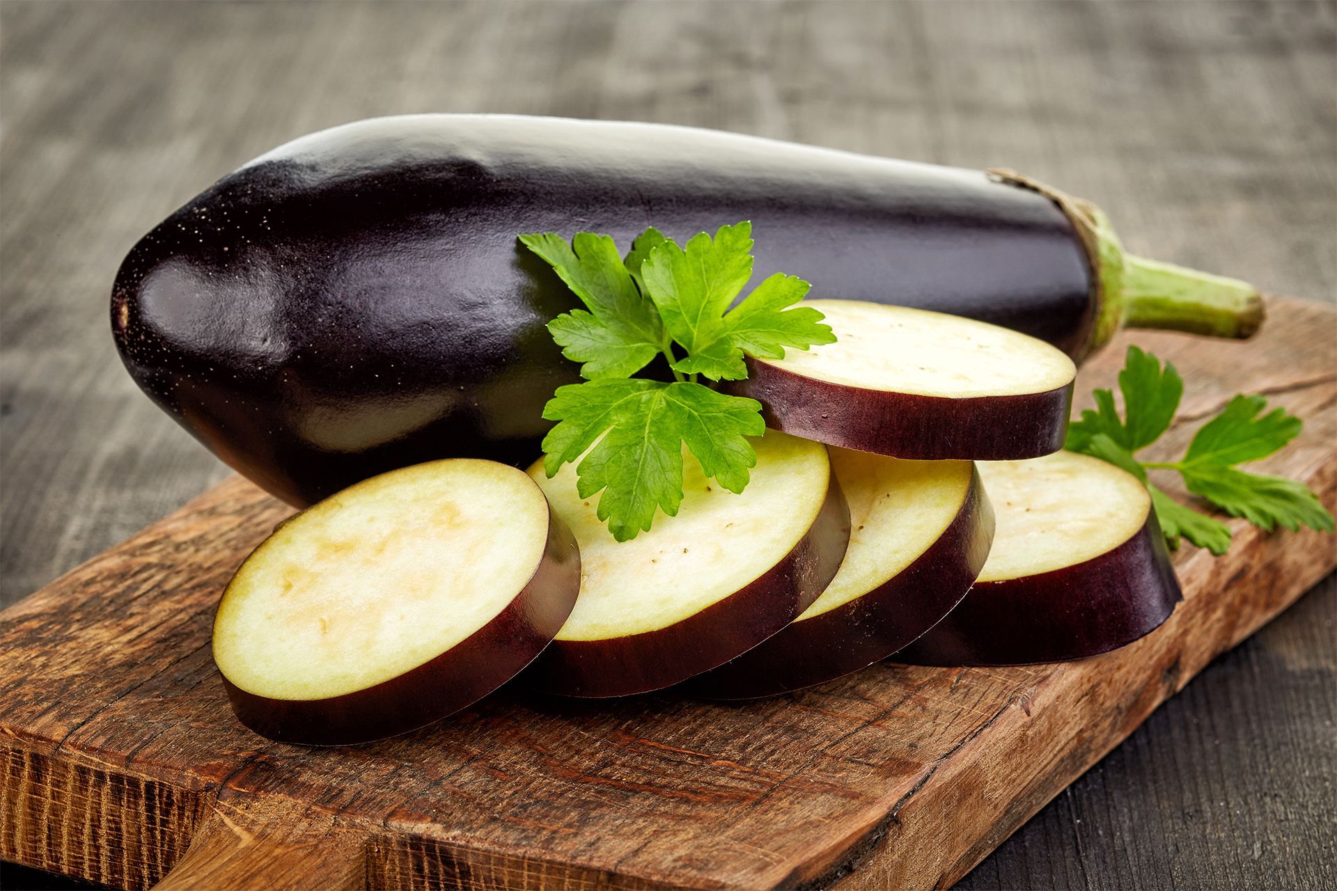 Sliced eggplant on a wooden board, garnished with parsley. Sliced eggplant on a wooden board, garnished with parsley.