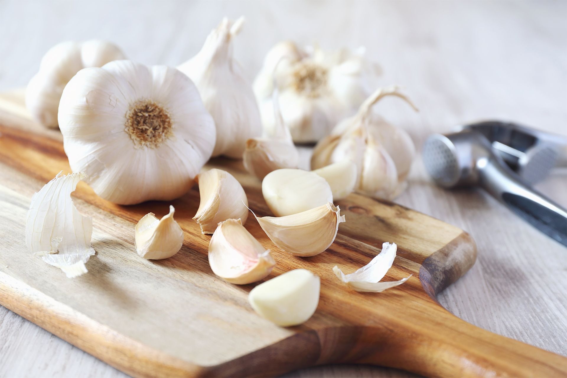 Garlic bulbs and peeled cloves on a wooden cutting board with a knife nearby. Garlic bulbs and peeled cloves on a wooden cutting board with a knife nearby.