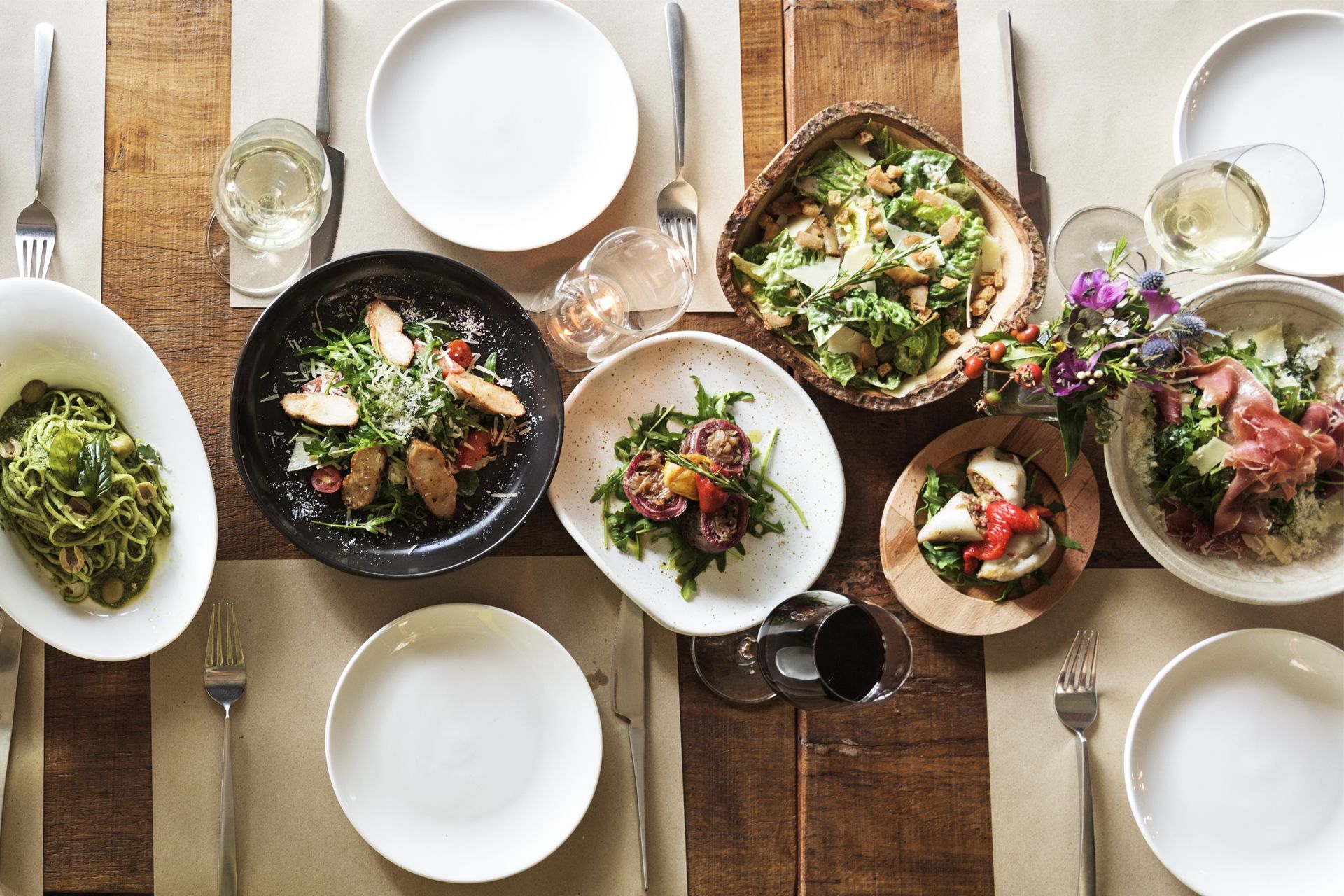 Overhead view of a rustic table set with assorted salads, plates, glasses, and silverware. Overhead view of a rustic table set with assorted salads, plates, glasses, and silverware.