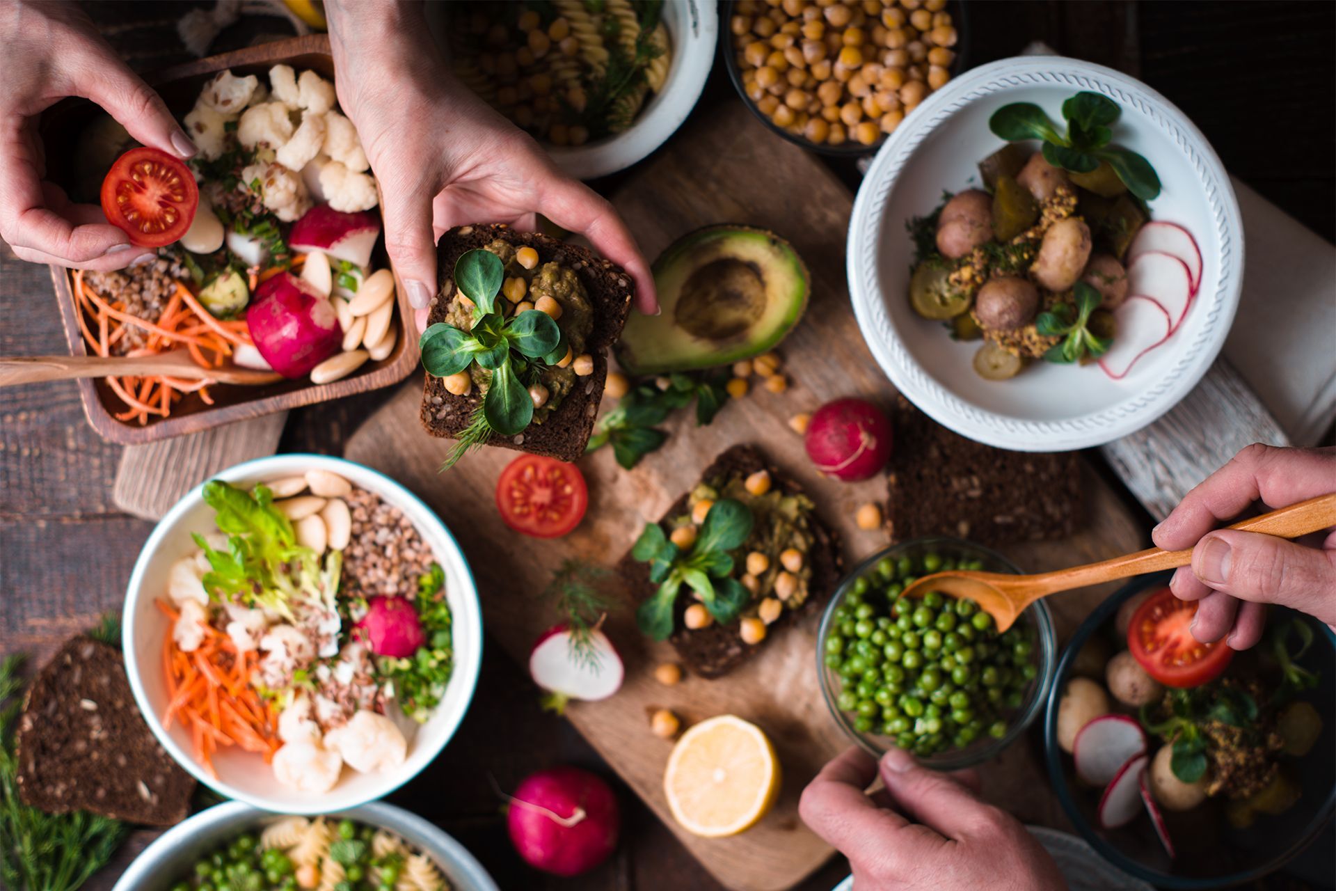 Hands preparing colorful salad bowls with vegetables and fruit on a rustic table.