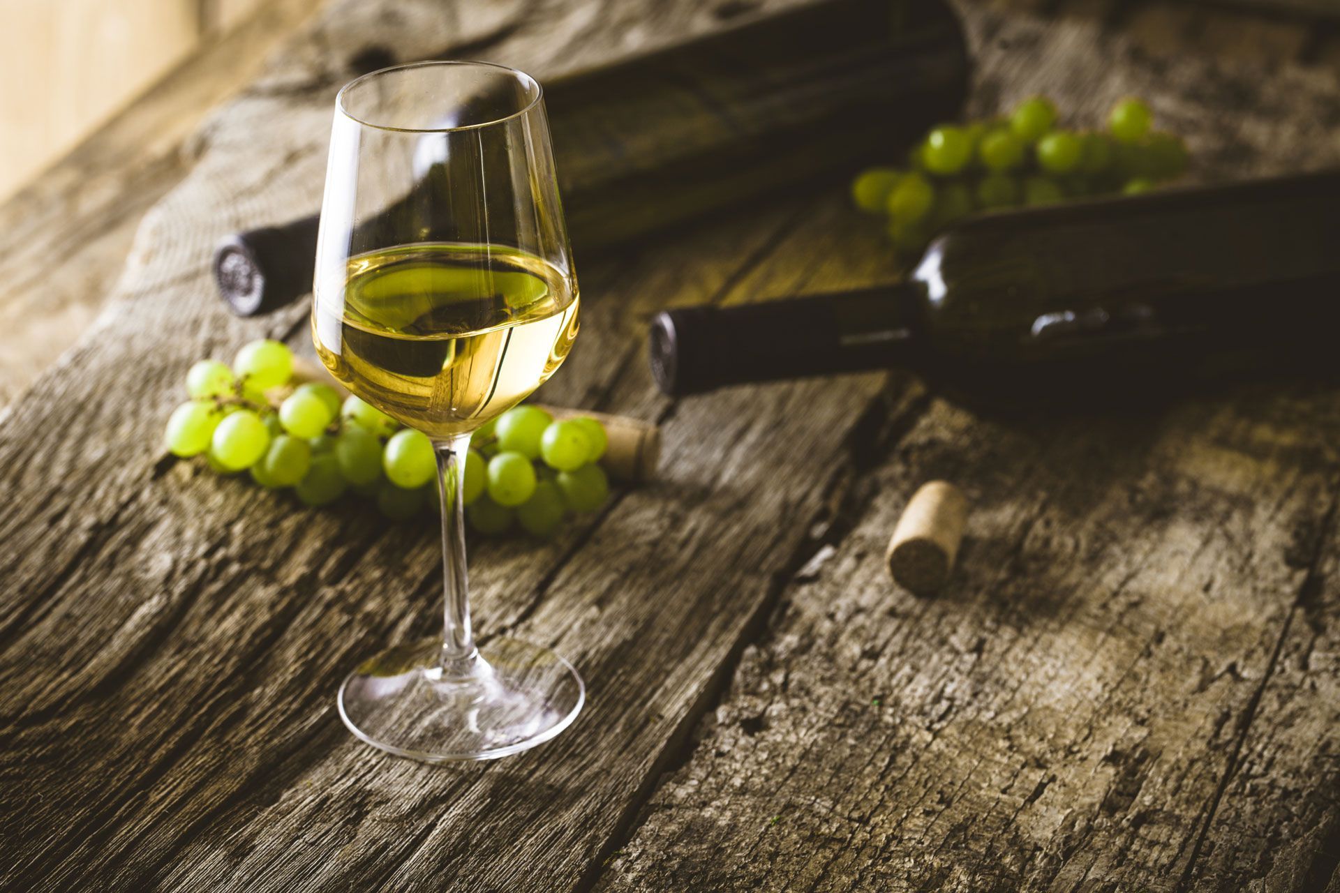 Wine glass with white wine, green grapes, and a wine bottle on a rustic wooden table