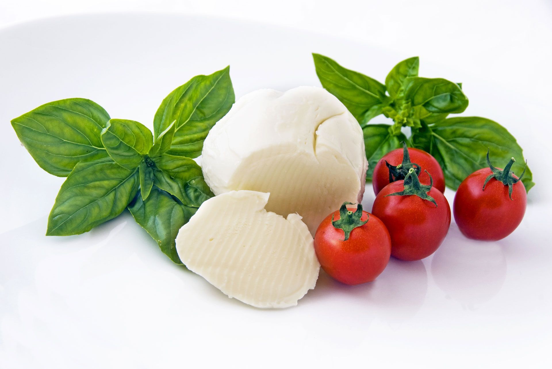 Fresh basil, mozzarella cheese, and red cherry tomatoes on a white background