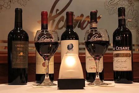 Five wine bottles on a table, including two filled glasses and a glowing center bottle display