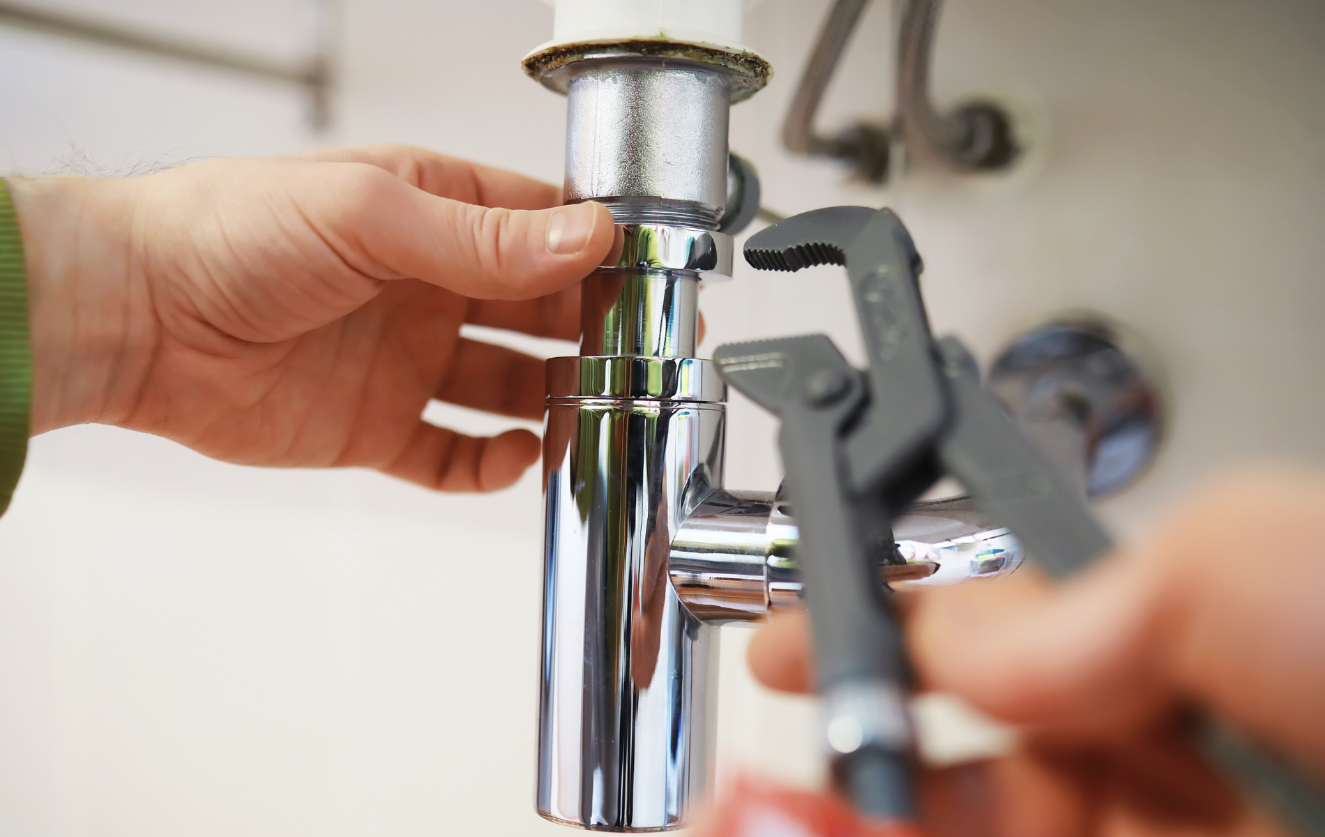 Person tightening sink pipe with wrench.