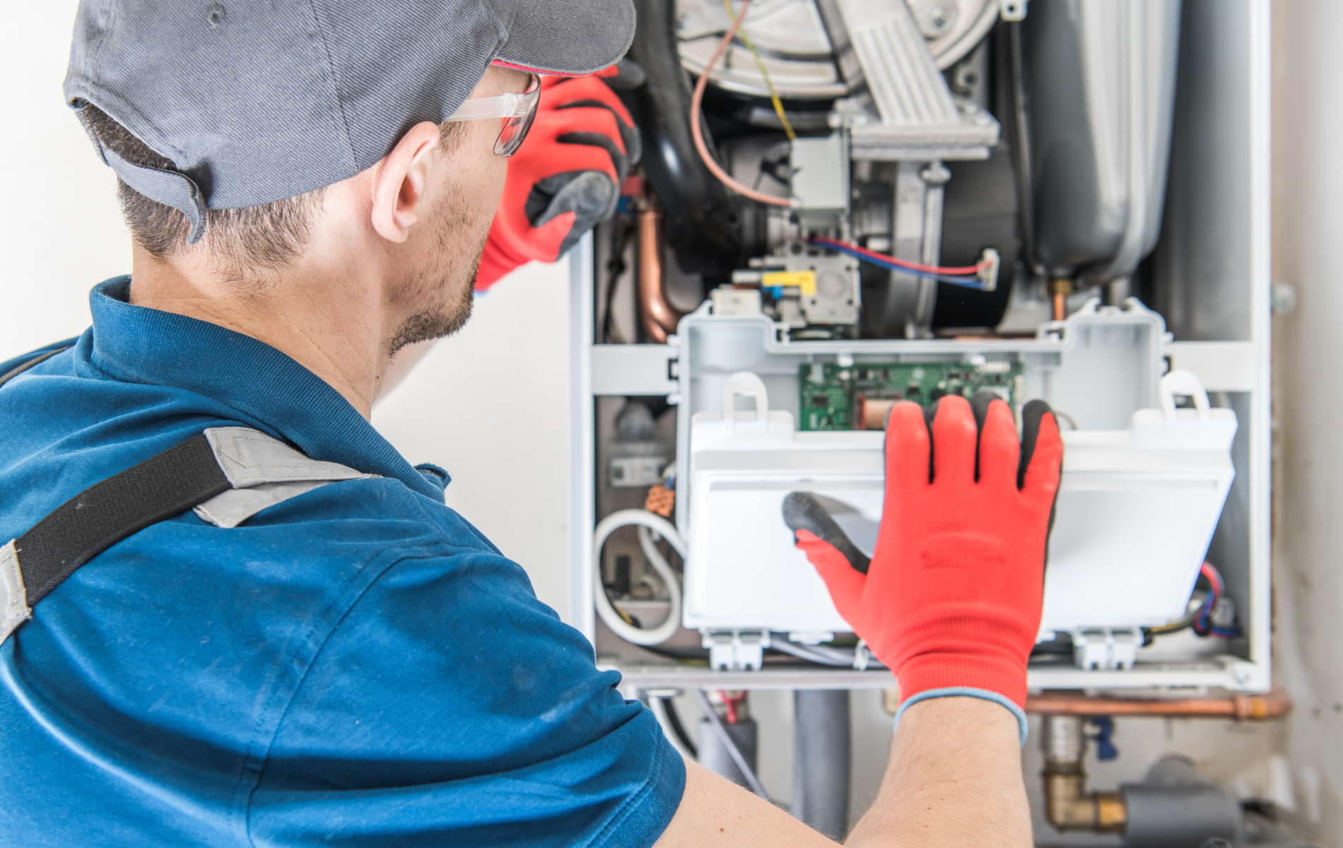 A repairman in red gloves repairs a heating system, examining the internal components.