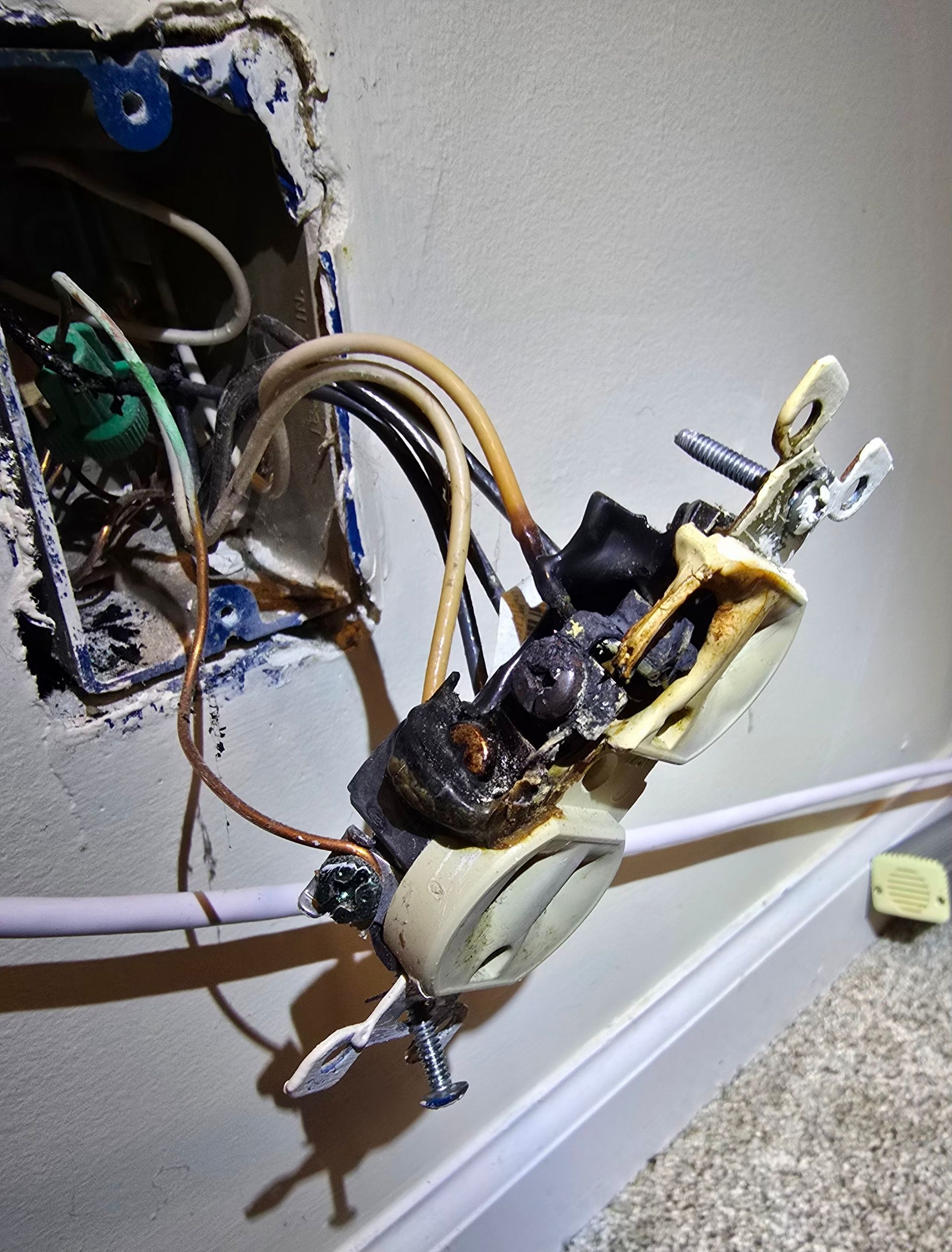 Exposed electrical outlet with a loose, burnt wiring device hanging from the wall box