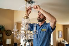 Technician installing a crystal chandelier in a living room ceiling