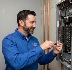 Man in a blue shirt tightening wiring inside an open electrical panel
